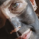 A woman applying a charcoal mask, enhancing skin rejuvenation.