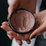 Hands holding a container of skincare cream, perfect for beauty and anti-aging products.