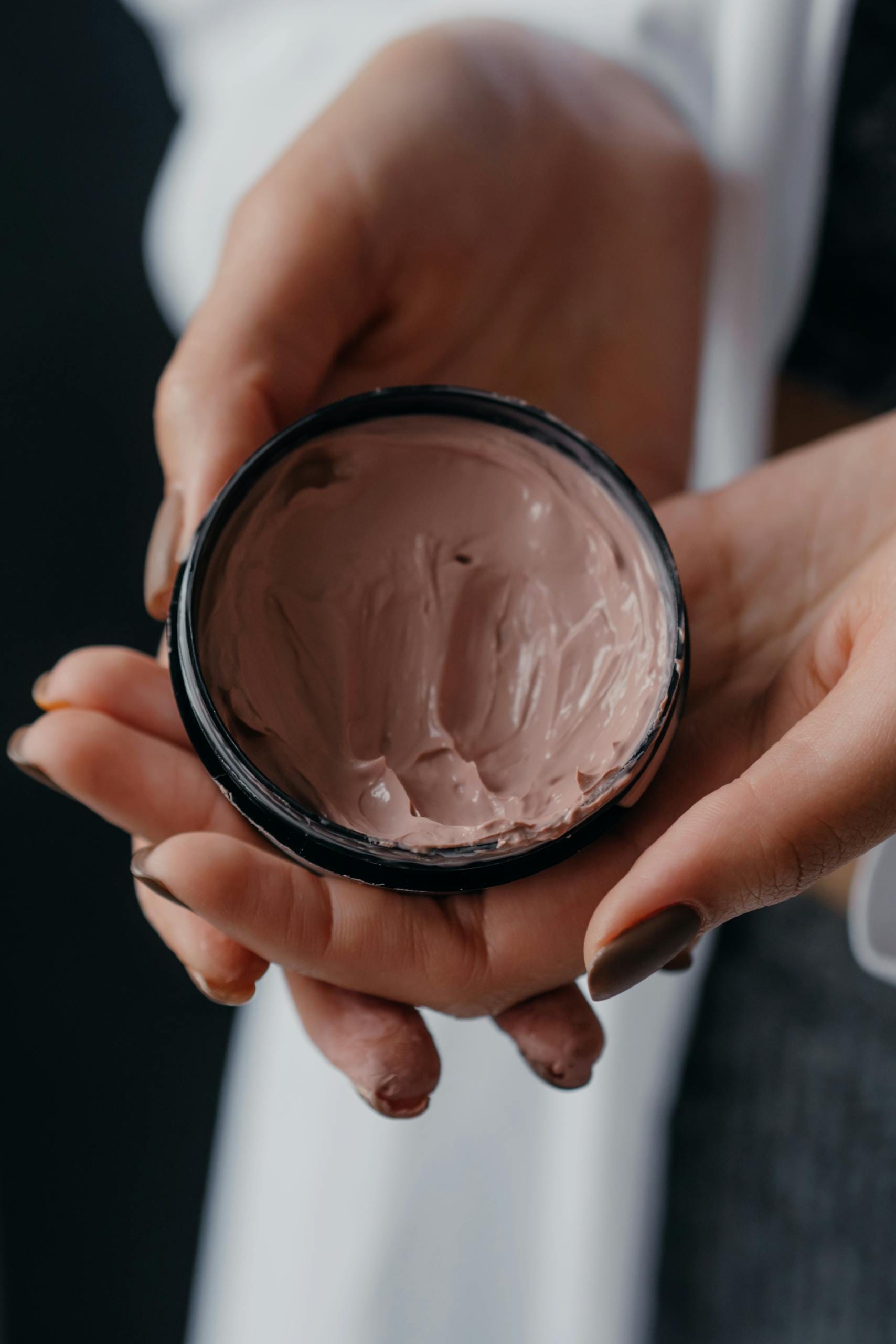 Hands holding a container of skincare cream, perfect for beauty and anti-aging products.