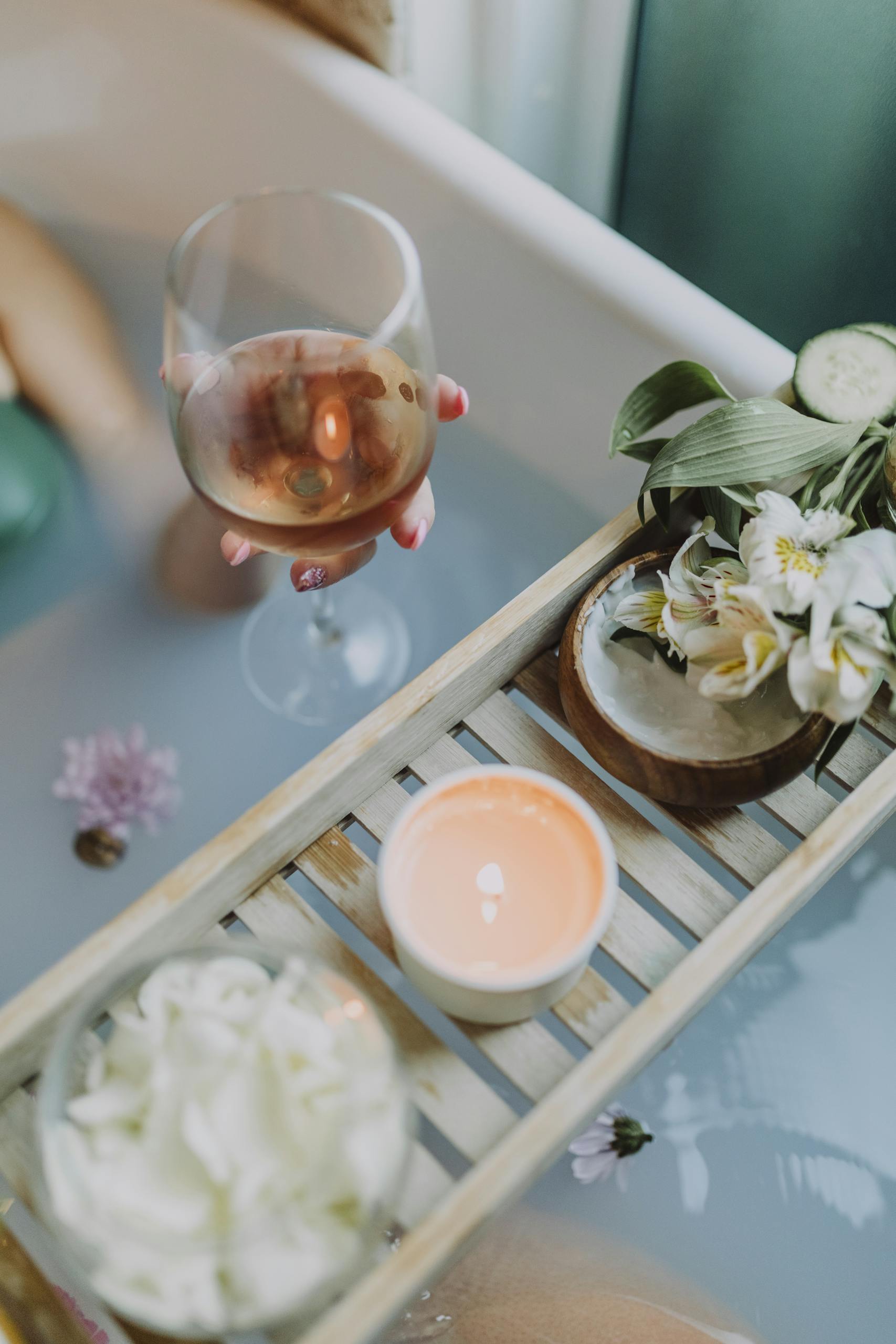 A serene bath setting with wine, candles, and flowers for a relaxing spa experience.