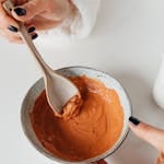 Hands mixing clay face mask in a ceramic bowl, highlighting skincare routine.
