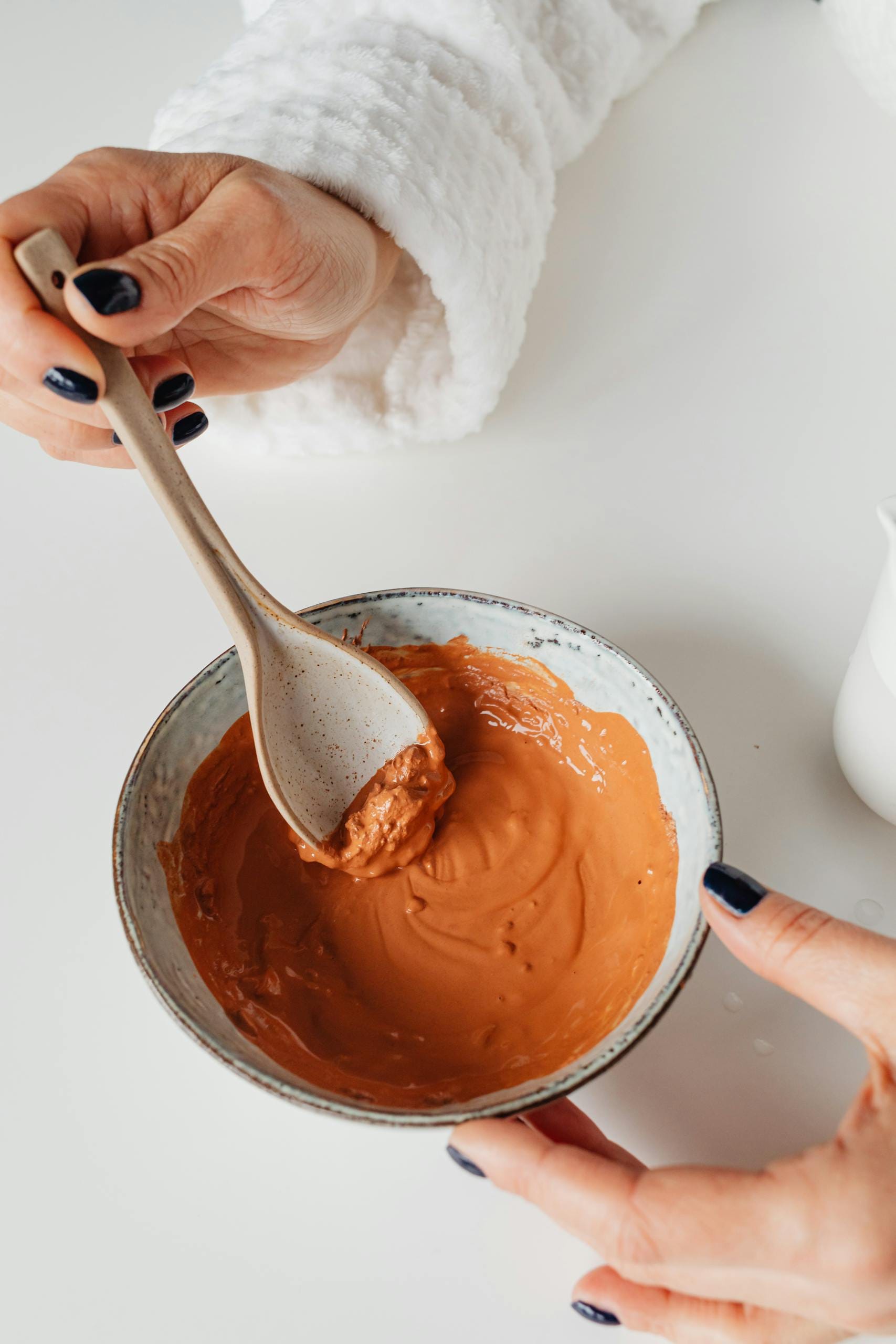 Hands mixing clay face mask in a ceramic bowl, highlighting skincare routine.