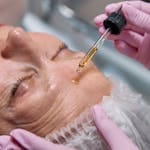 Senior woman receiving a facial serum treatment in a spa setting.