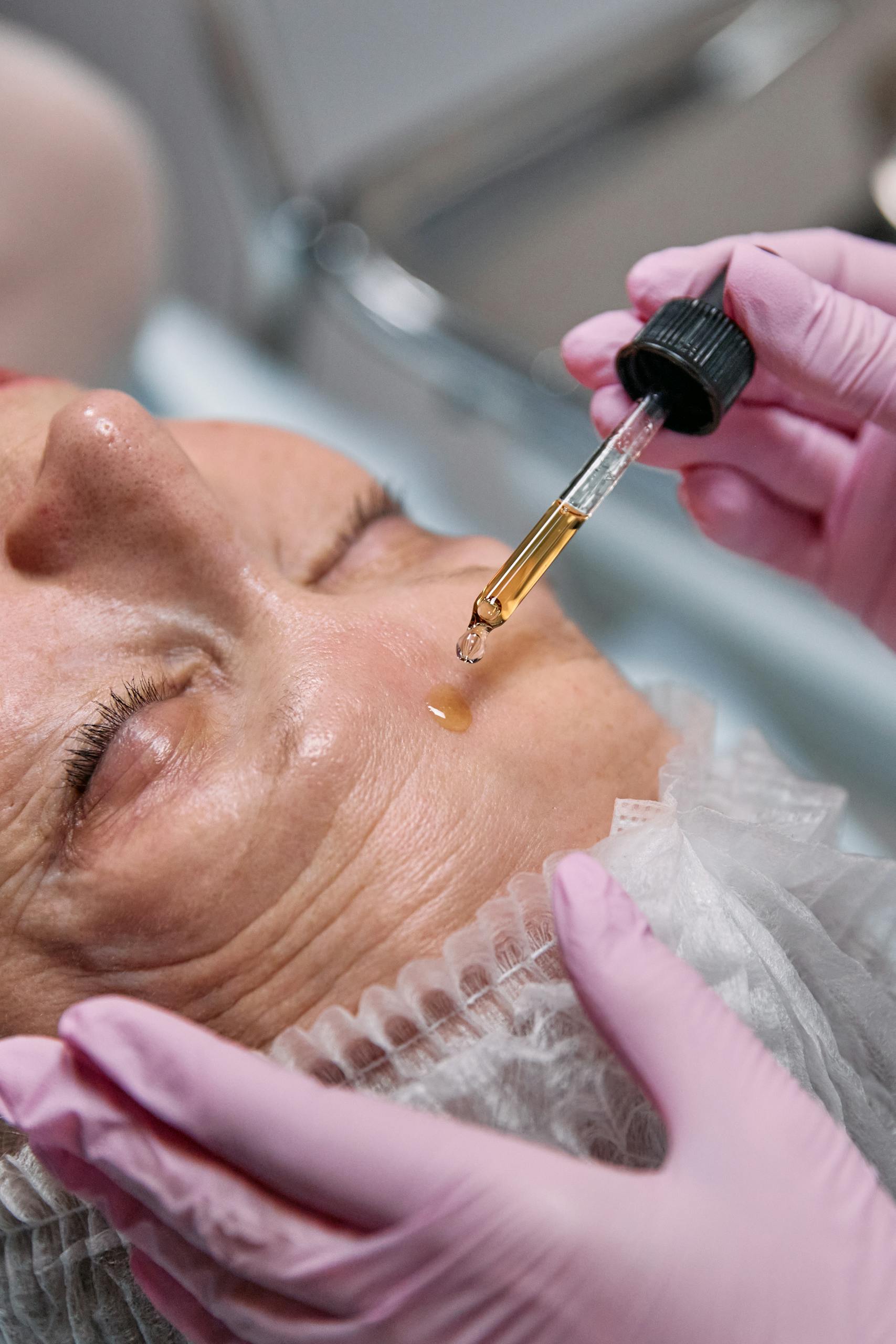 Senior woman receiving a facial serum treatment in a spa setting.