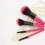 Pink and black makeup brushes arranged on pearl necklace for elegant look.