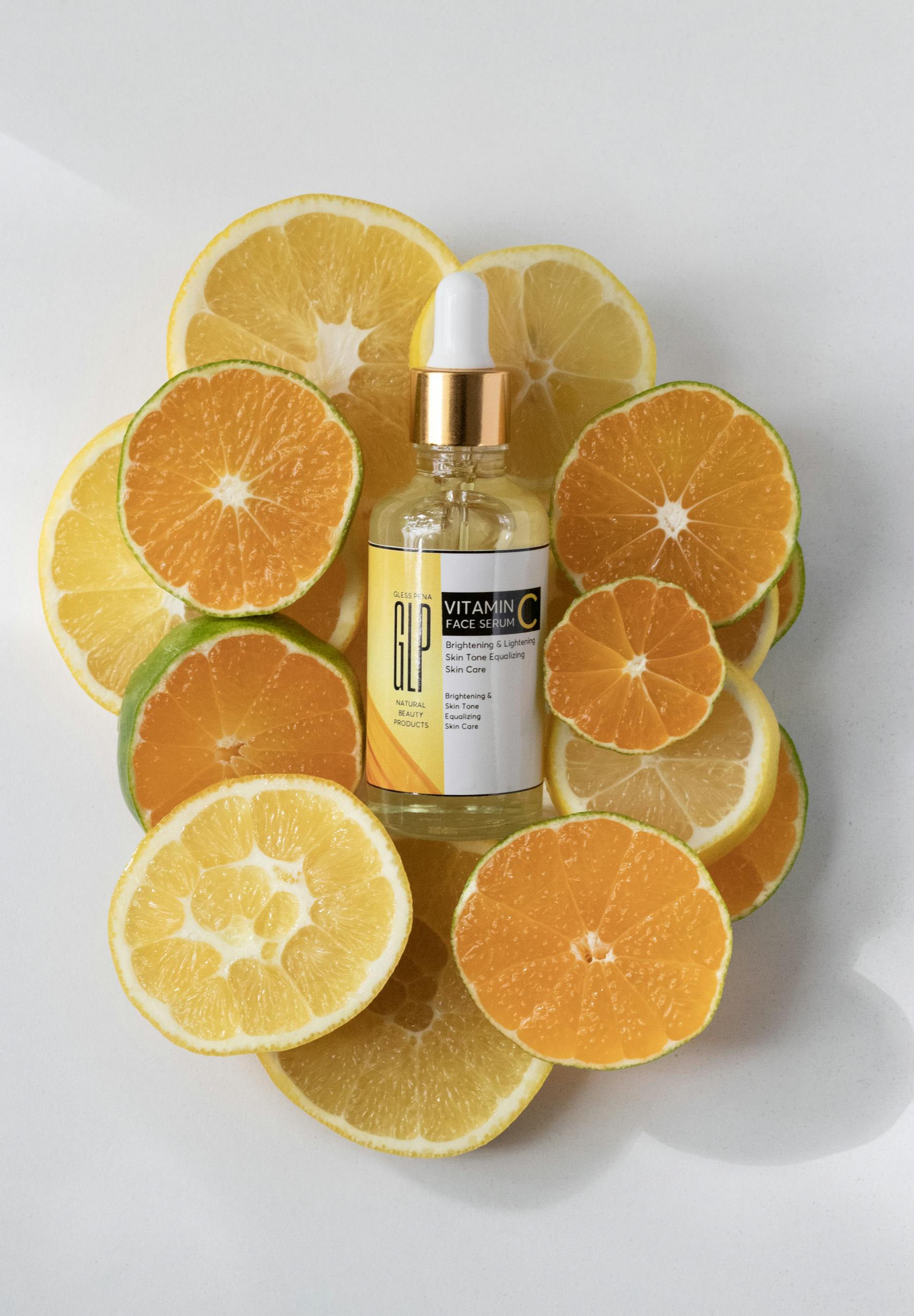 Vitamin C serum bottle surrounded by fresh orange and lemon slices.
