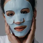 A close-up portrait of a woman wearing a blue skincare face mask, emphasizing self-care and beauty.