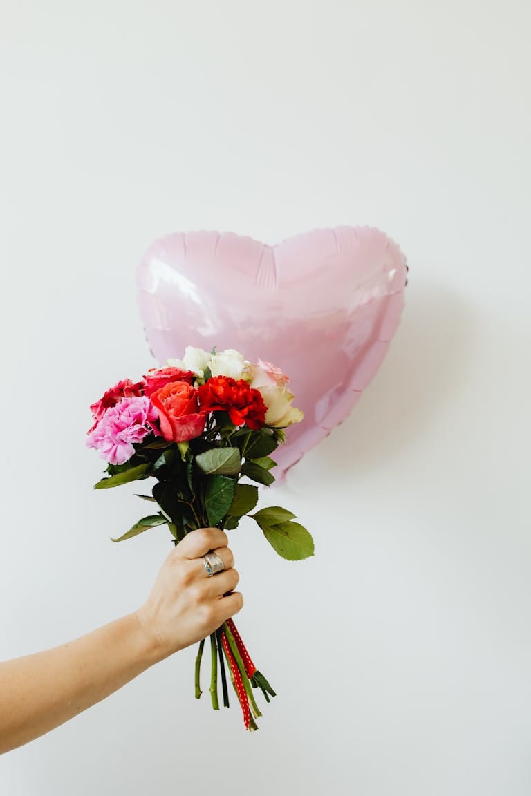 A hand holding a vibrant bouquet and heart-shaped balloon, perfect for romantic occasions.