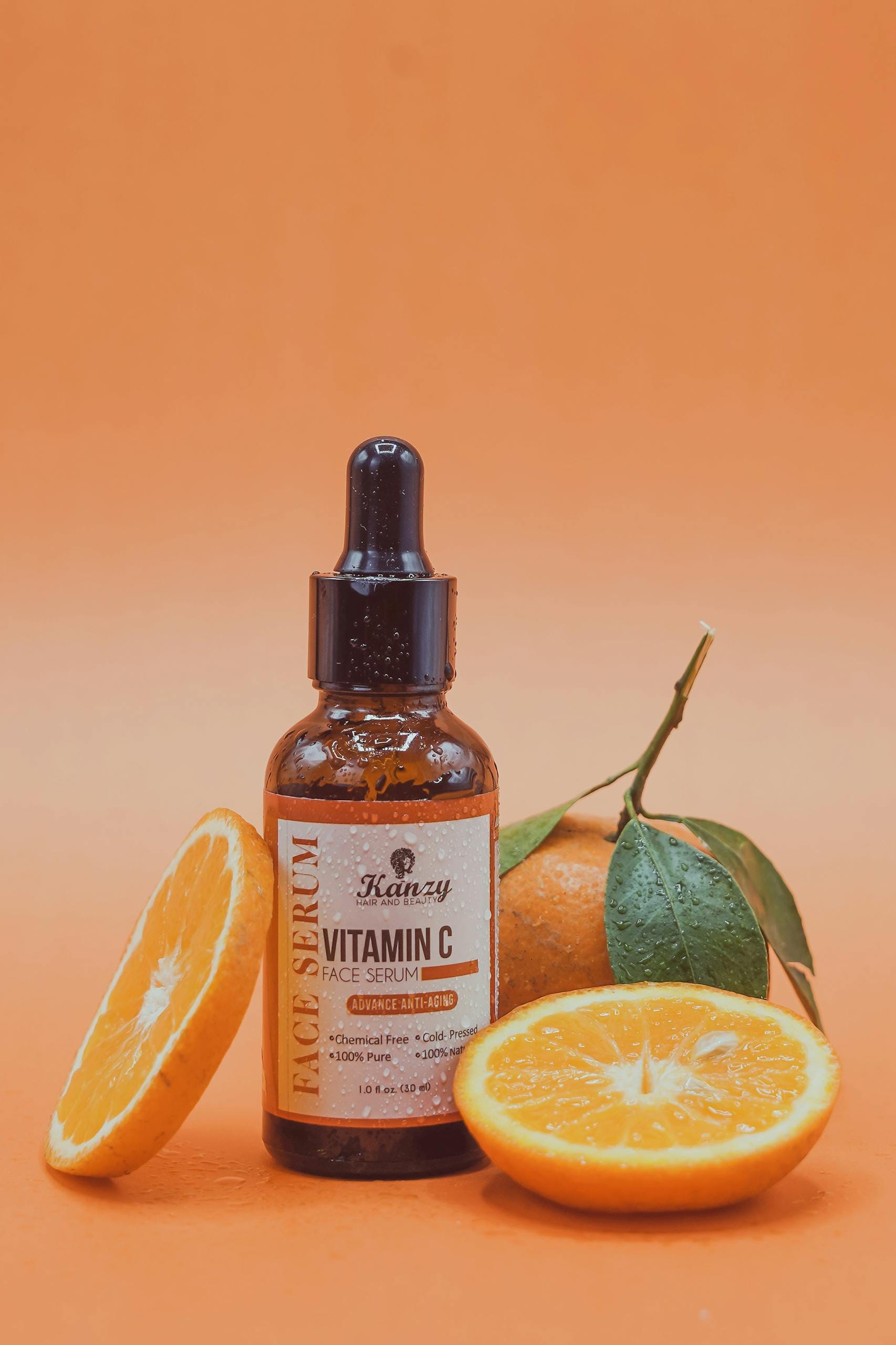 Face serum with vitamin C and orange slices on orange background for skincare.