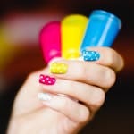 Close-up of colorful polka dot nail art on hand, showcasing pink, yellow, and blue shades.