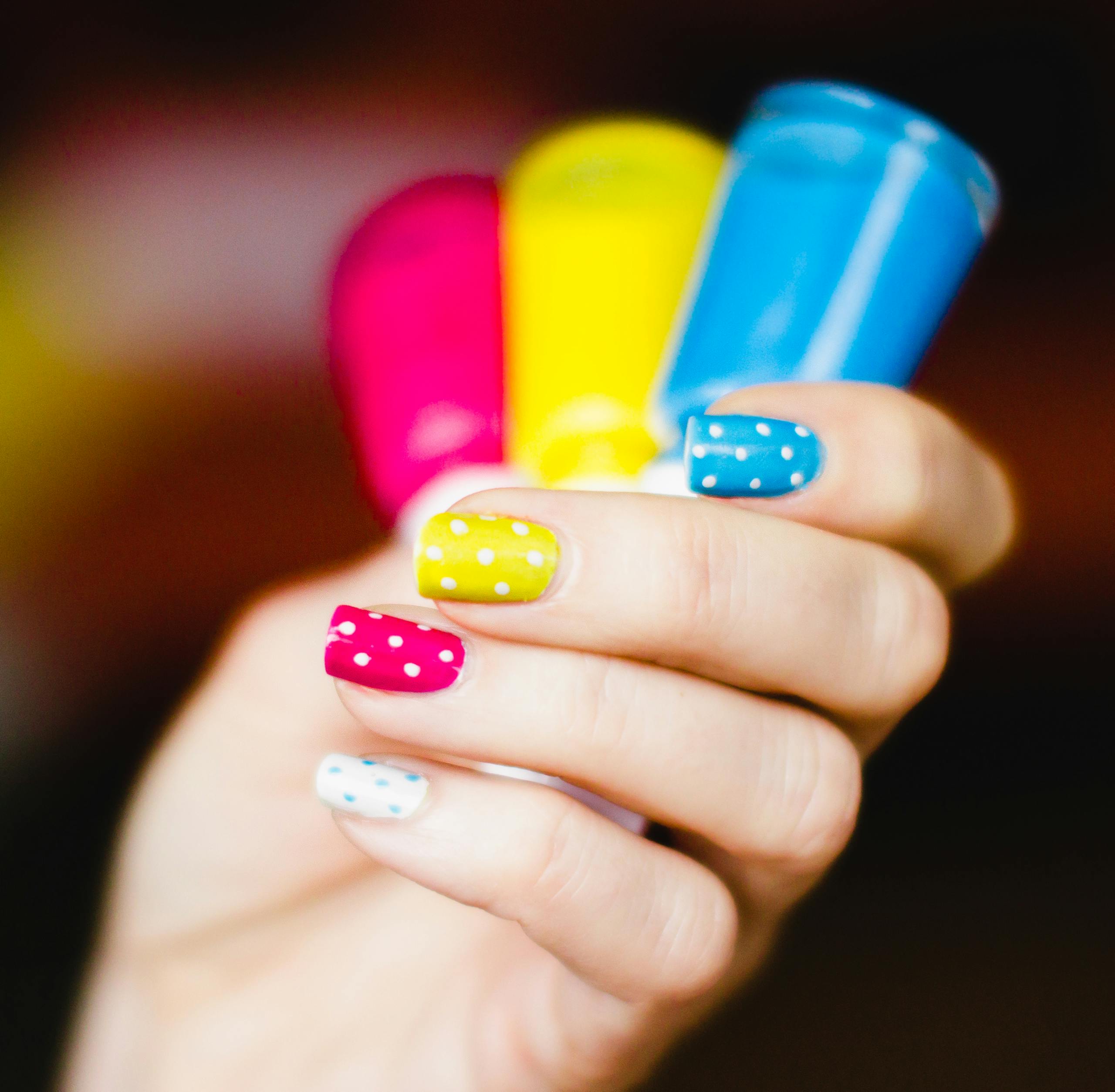 Close-up of colorful polka dot nail art on hand, showcasing pink, yellow, and blue shades.