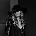 A fashionable woman in chic attire and hat, captured in a stylish black and white portrait.