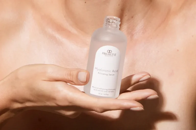 Woman examining her skin in a modern bathroom mirror with a minimal selection of skincare products beside her